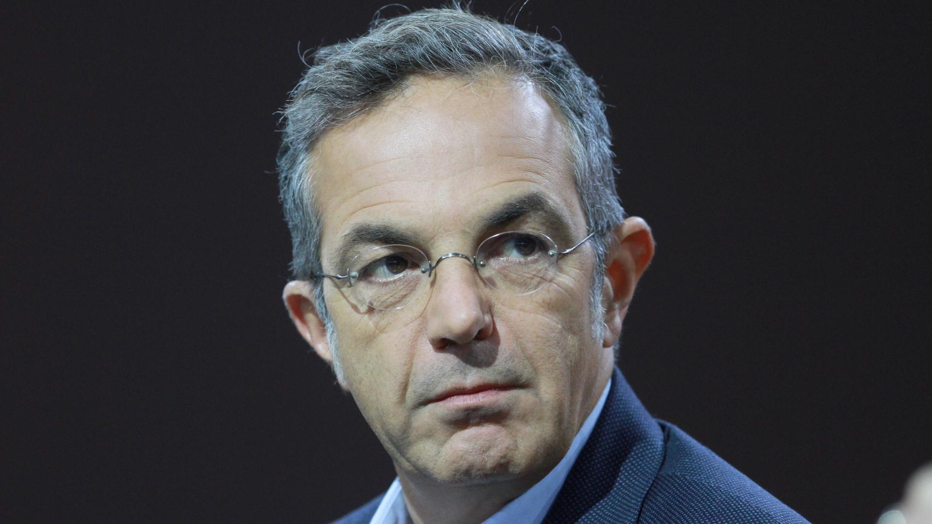 Navid Kermani, mit Brille, in einem blauen Sakko, sitzt auf einem Podium. 