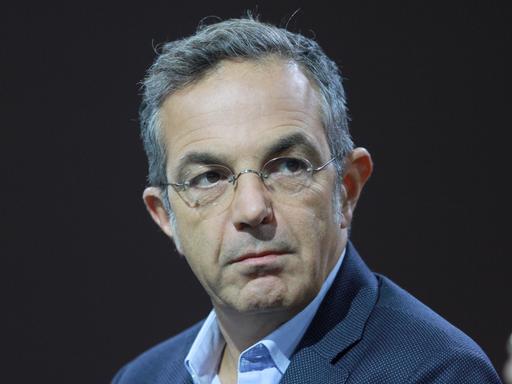 Navid Kermani, mit Brille, in einem blauen Sakko, sitzt auf einem Podium. 