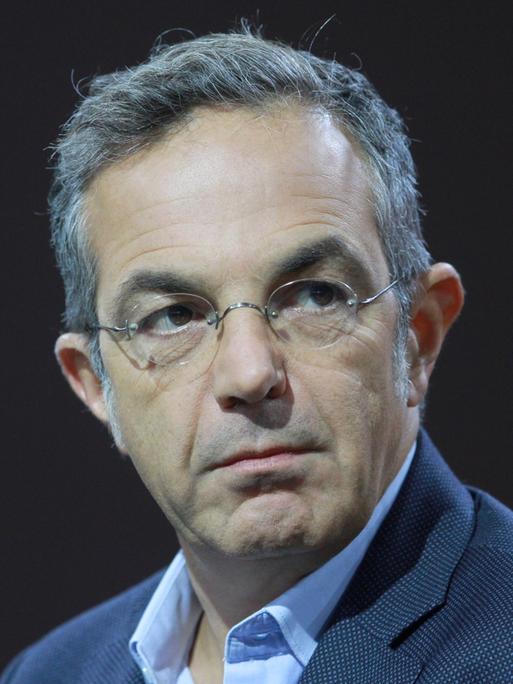 Navid Kermani, mit Brille, in einem blauen Sakko, sitzt auf einem Podium. 