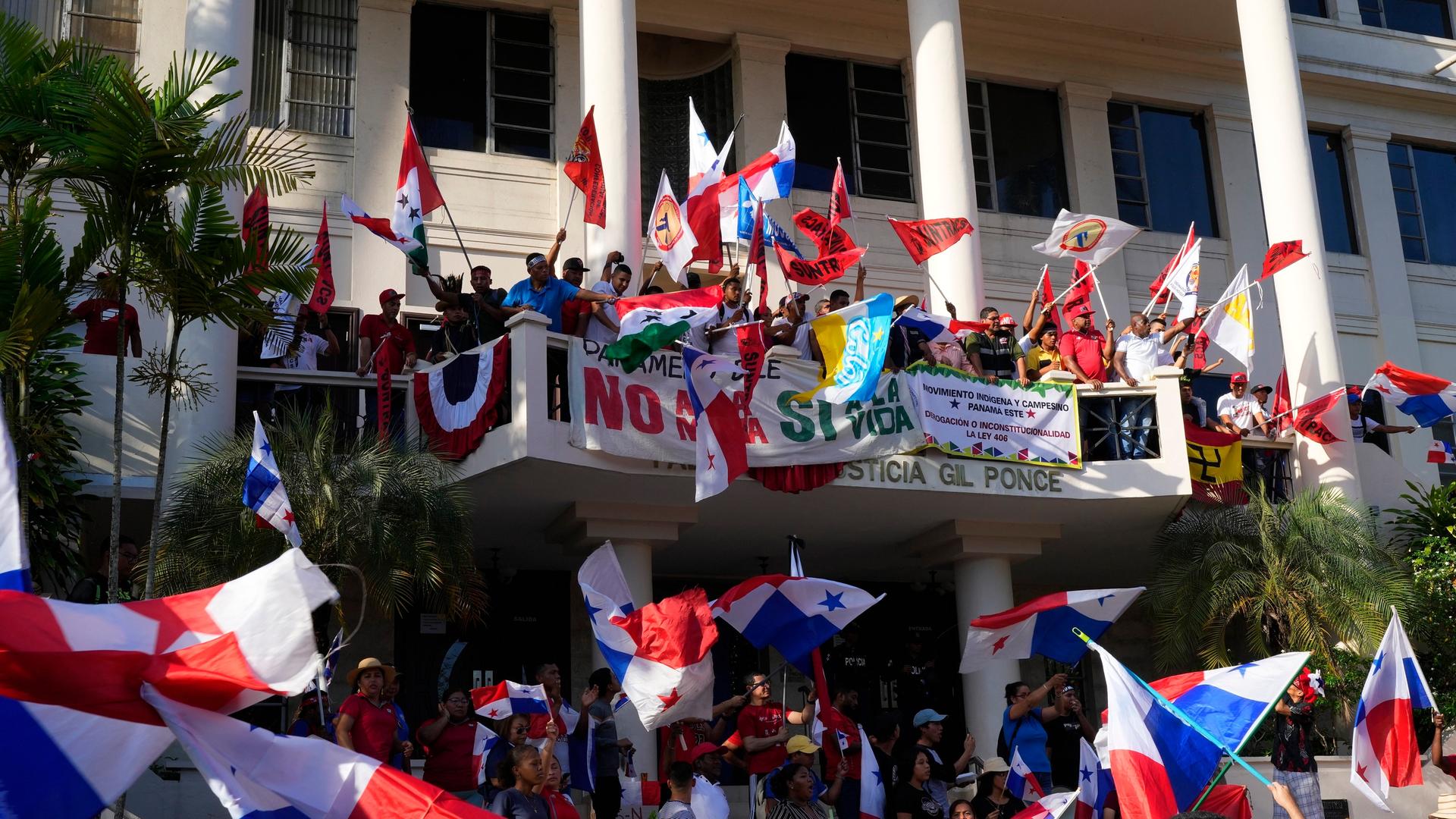 Zu sehen sind Demonstranten vor einem Haus in Panama-Stadt, die Fahnen schwenken. Auf dem Balkon sind mehrere Transparente angebracht.