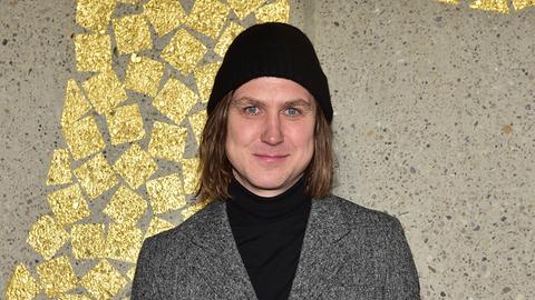 Lars Eidinger vor einer gold verzierten Wand anläßlich der Verleihung der Insignien eines Ritters der Arts et Lettres  in der Französischen Botschaft Berlin.