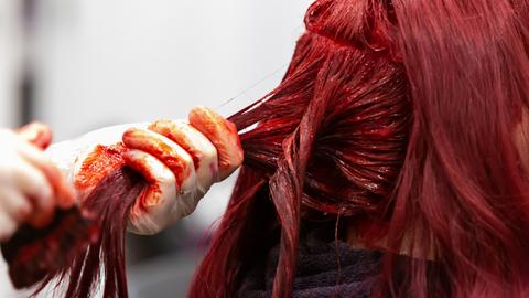 Friseurbesuch: Nahaufnahme einer Hand mit Latex-Handschuh, die einer Frau rote Haarfarbe einmassiert.