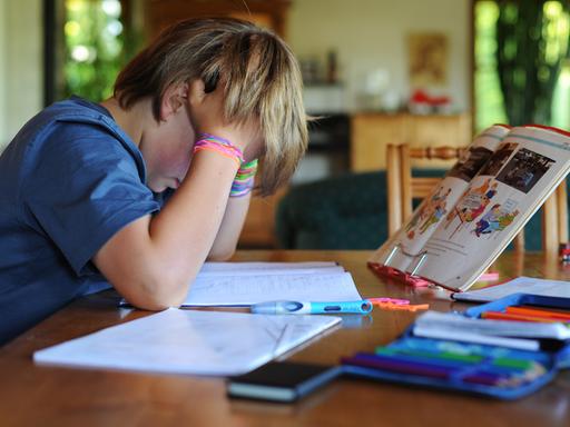 Ein Junge hält beim Erledigen seiner Hausaufgaben seinen Kopf in den Händen.