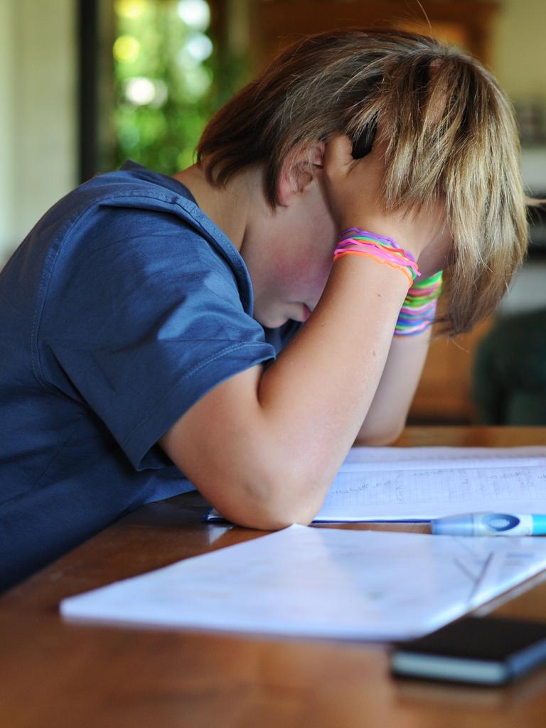 Ein Junge hält beim Erledigen seiner Hausaufgaben seinen Kopf in den Händen.