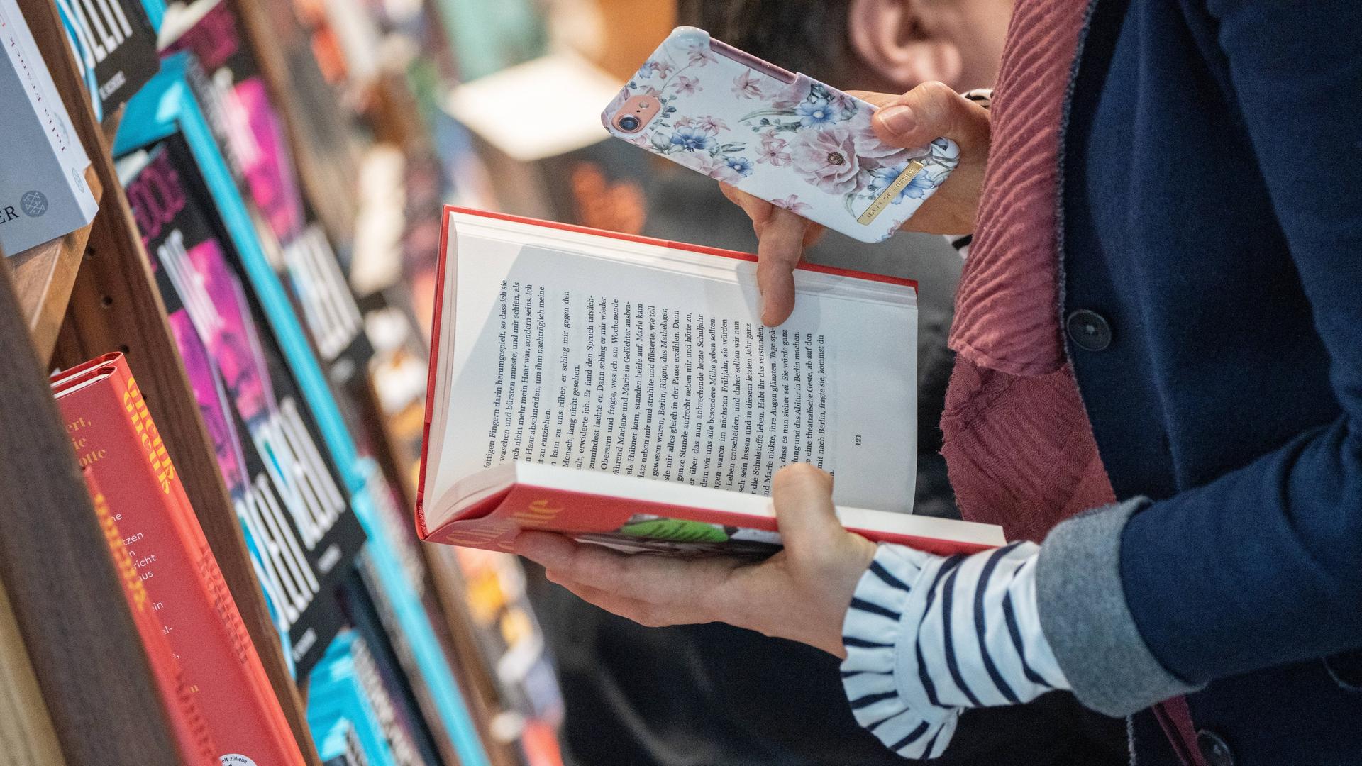 Zwei Hände halten ein Buch und ein Smartphone (auf der Leipziger Buchmesse 2024)