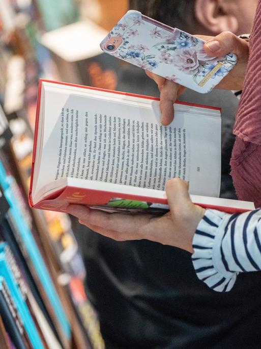 Zwei Hände halten ein Buch und ein Smartphone (auf der Leipziger Buchmesse 2024)