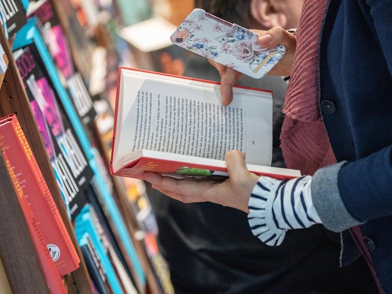 Zwei Hände halten ein Buch und ein Smartphone (auf der Leipziger Buchmesse 2024)