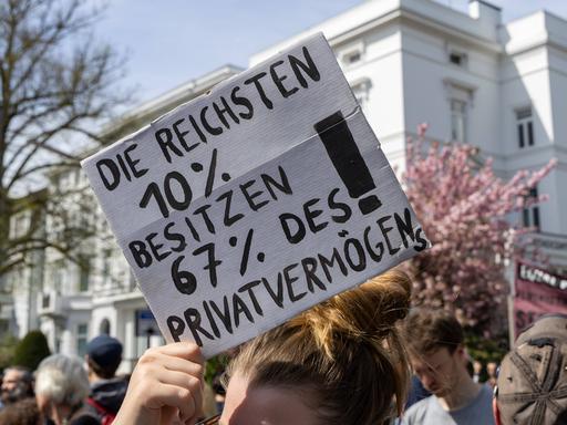 1. Mai-Demonstration unter dem Motto "Wer hat, der gibt" in Hamburg 2023. In Hamburgs teurem Wohnviertel Pöseldorf machten etwa 2700 Demonstrierende auf soziale Ungerechtigkeit aufmerksam. Eine Frau hält ein Schild hoch: Die reichsten 10 % besitzen 67 % des Privatvermögens.