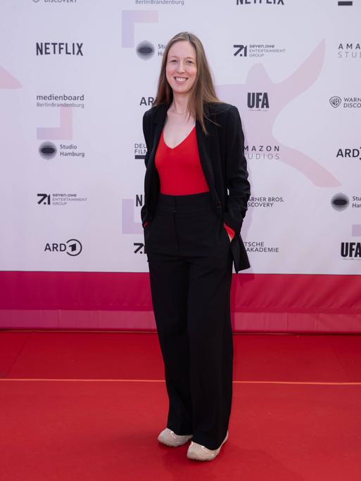 Kamerafrau Caroline Spreitzenbart steht vor einer Sponsorenwand, wie sie bei Filmfestivals üblich ist.