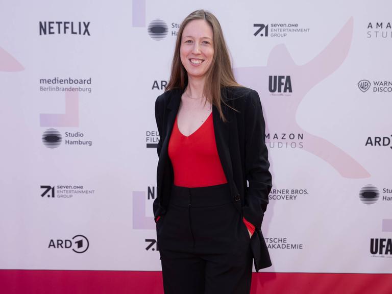 Kamerafrau Caroline Spreitzenbart steht vor einer Sponsorenwand, wie sie bei Filmfestivals üblich ist.