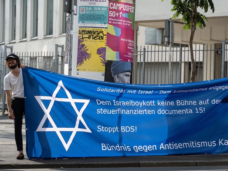 Juni 2022: Demonstranten stehen vor einer Podiumsveranstaltung der Bildungsstätte Anne Frank und der Trägergemeinschaft documenta gGmbH zum Thema "Antisemitismus in der Kunst. Auf einem Banner fordern sie Solidarität mit Israel und das Entgegentreten gegen Antisemitismus.  