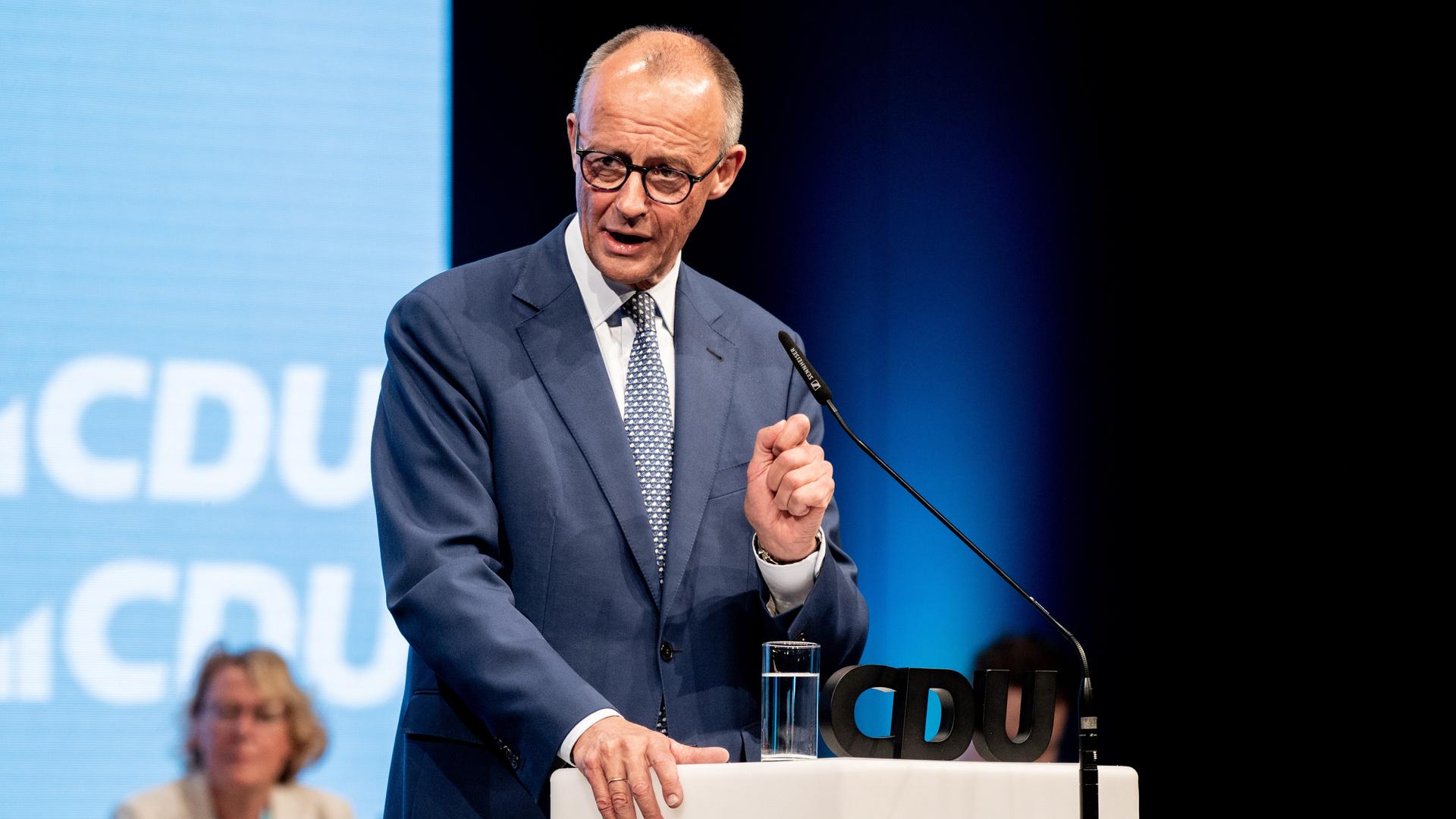 Friedrich Merz steht an einem Redepult und spricht zu den Delegierten. Im Hintergrund sind Logos der CDU mit weißer Schrift auf blauem Grund zu sehen. Friedrich Merz steht an einem Redepult und spricht zu den Delegierten. Im Hintergrund sind Logos der CDU mit weißer Schrift auf blauem Grund zu sehen.