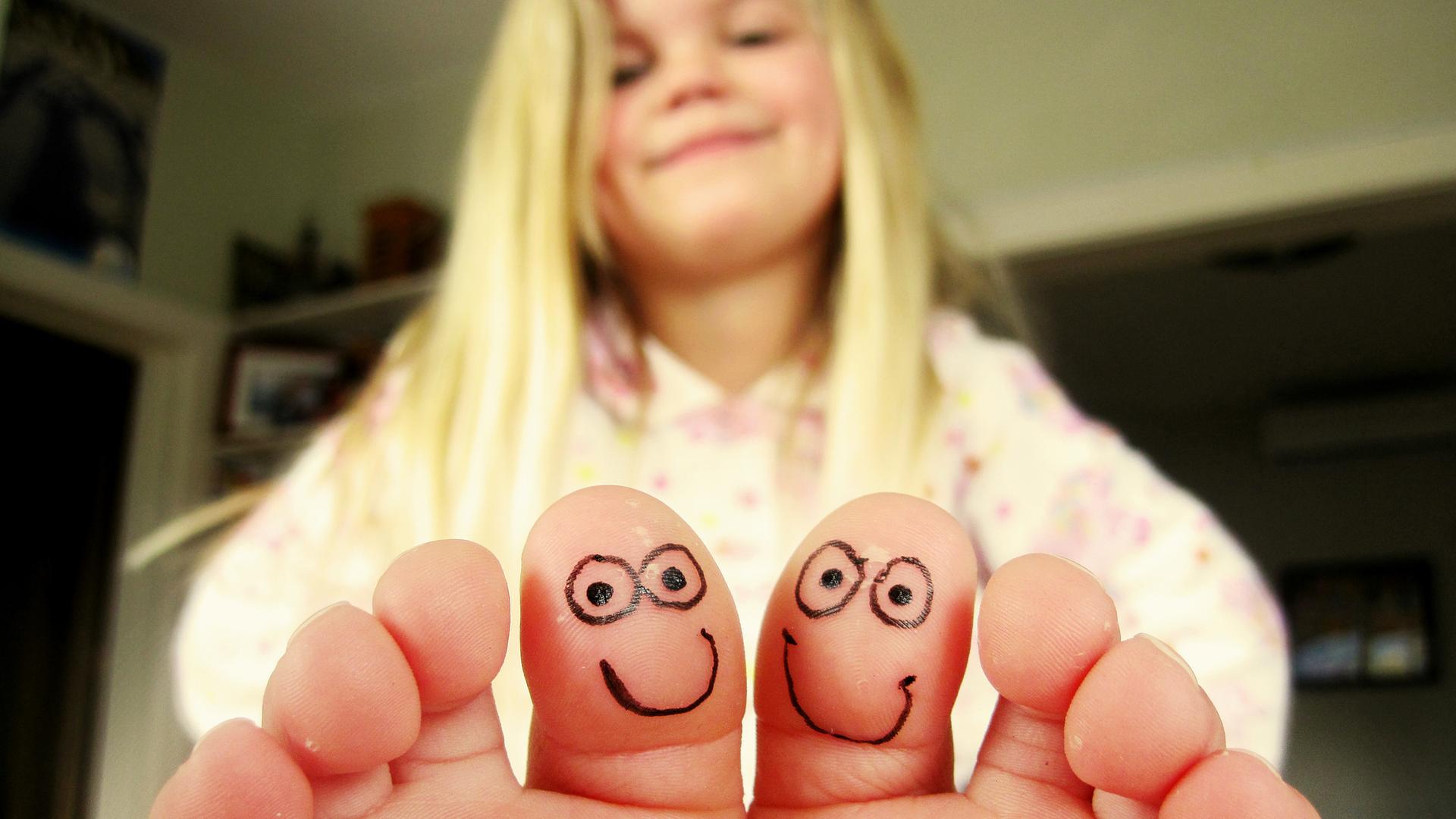 Ein Mädchen sitzt in einem Zimmer und hält ihre Zehen in die Kamera, die beiden großen Zehen sind mit kleinen gesichtern bemalt Ein Mädchen sitzt in einem Zimmer und hält ihre Zehen in die Kamera, die beiden großen Zehen sind mit kleinen gesichtern bemalt