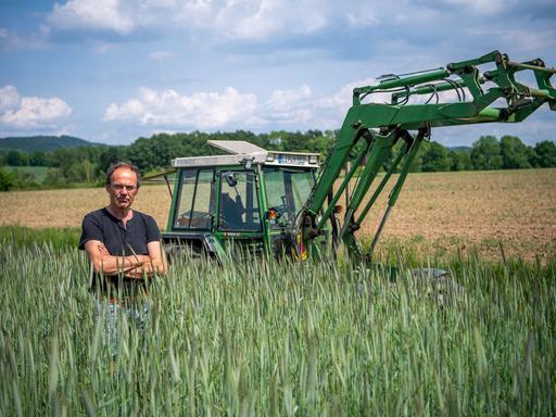 Ulf Allhoff-Cramer, Landwirt, steht in einem Roggen-Feld vor seinem Traktor. 