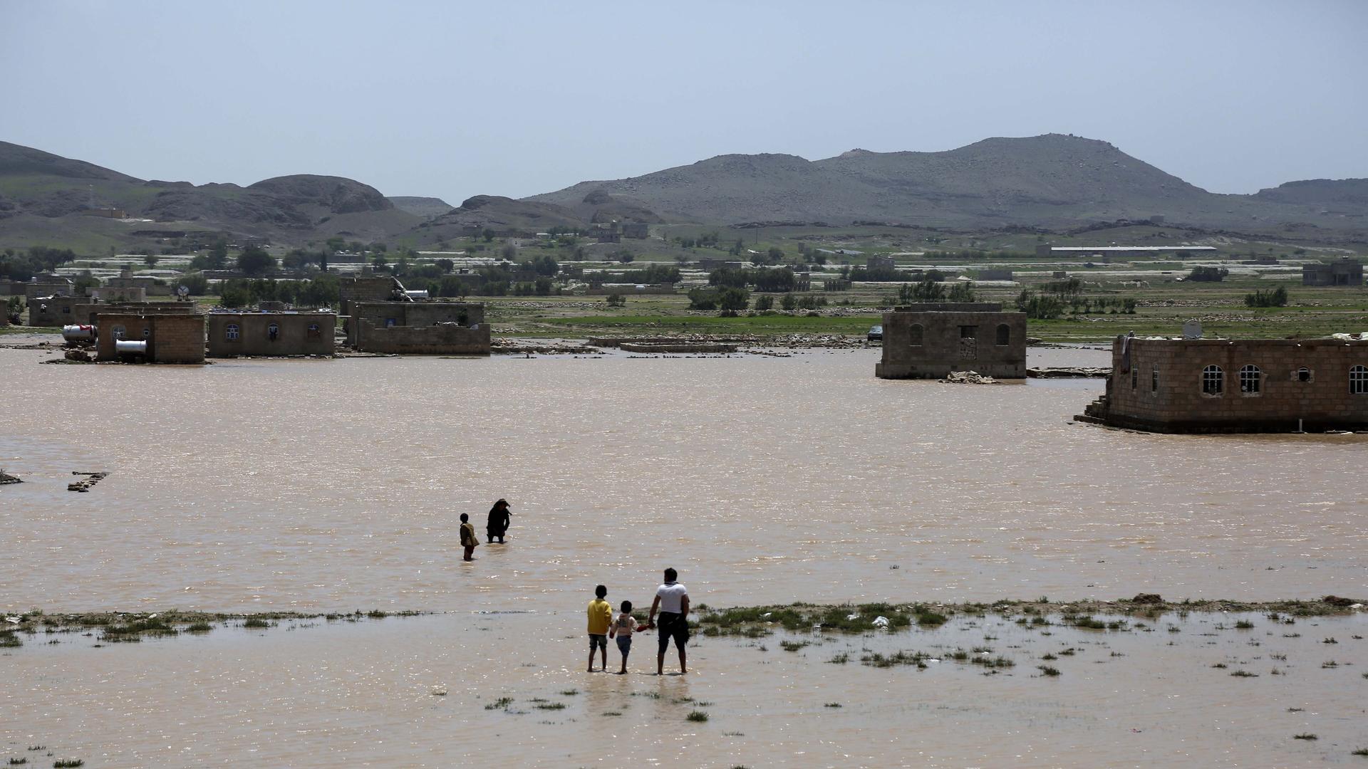 Blick über weites Land, welches durch Regen überschwemmt wurde. Vereinzelt stehen Menschen in der Landschaft.