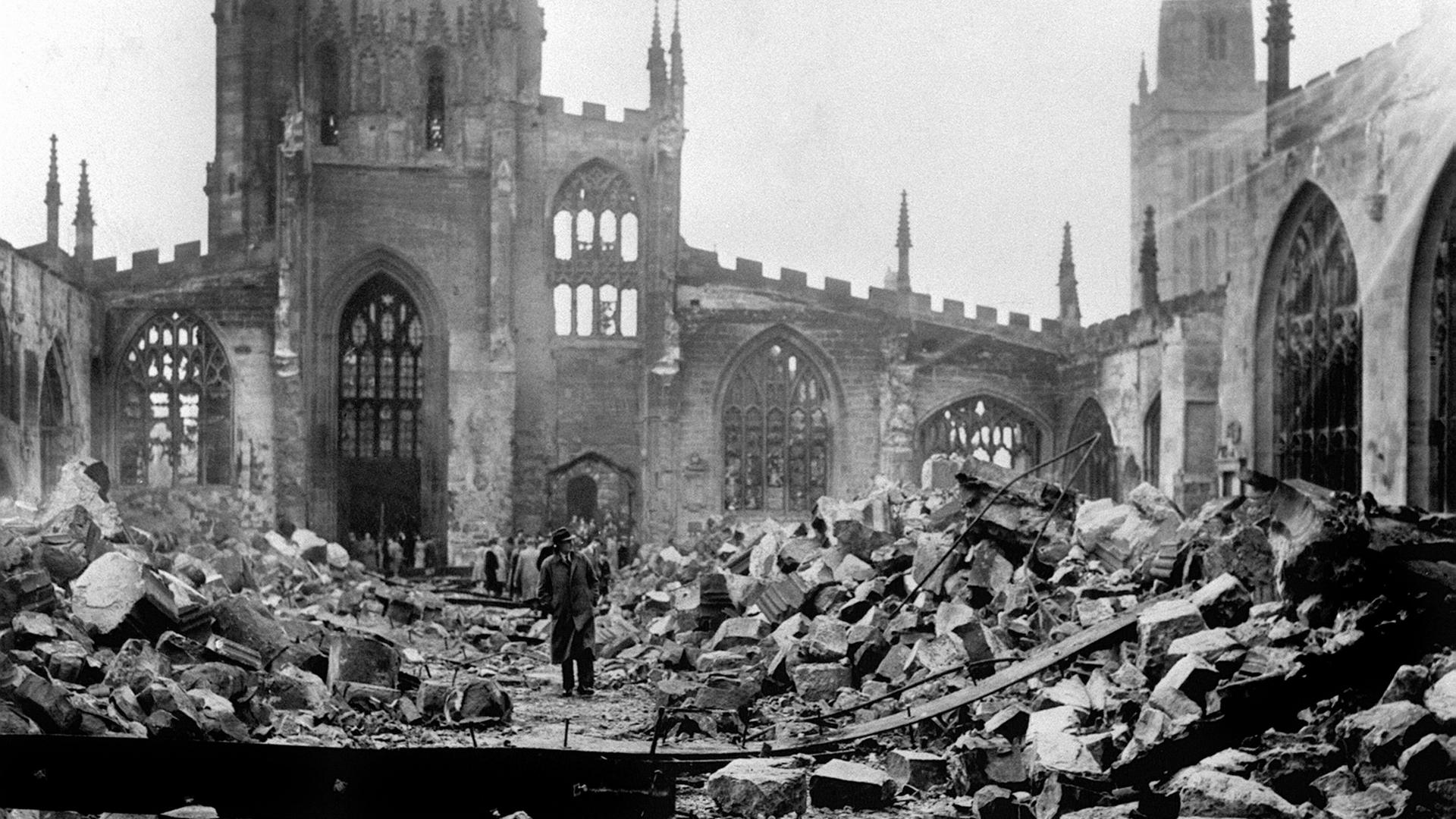 Ein Mann läuft durch die zerstörte Ruine der Kathedrale von Coventry am 14.11.1940. Das Foto ist in schwarz-weiß.
