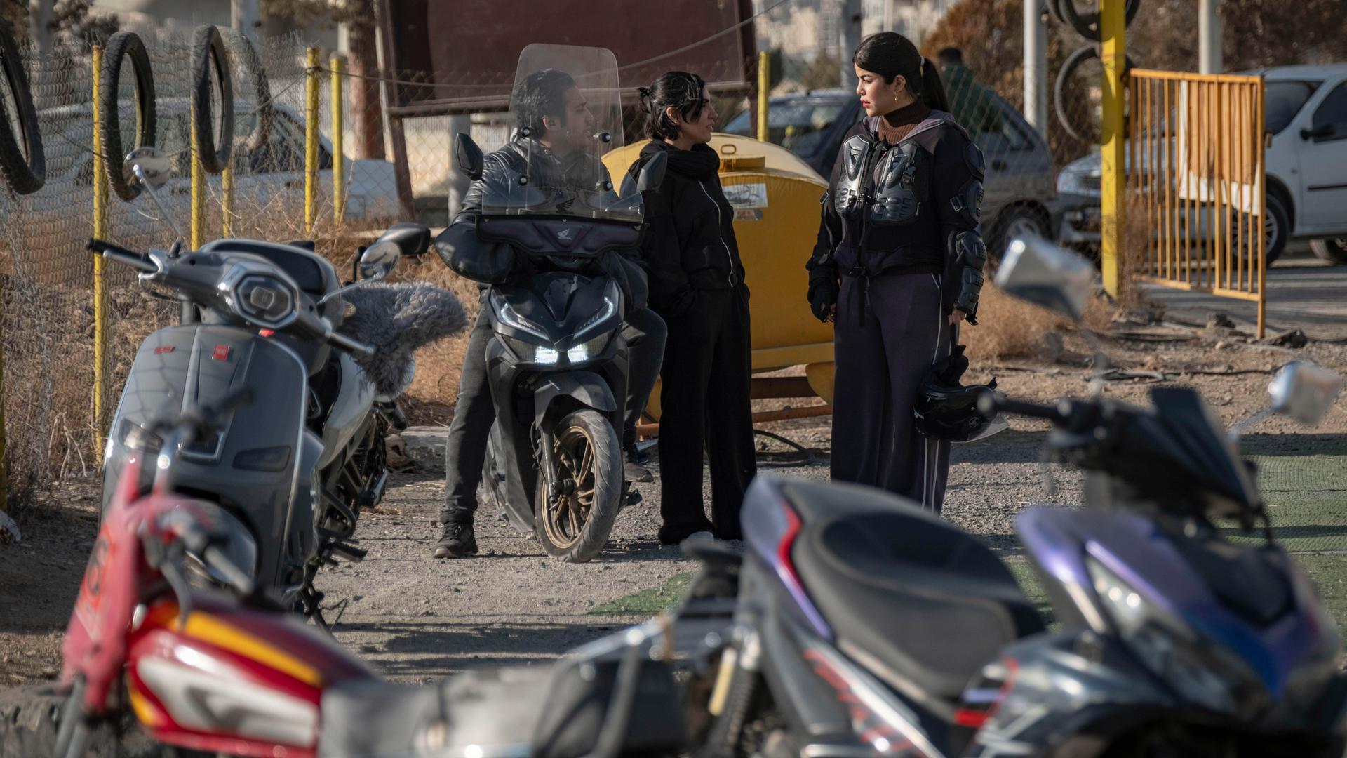 Mehrere junge iranische Frauen stehen zusammen und unterhalten sich. Im Vordergrund sieht man Motorräder stehen.