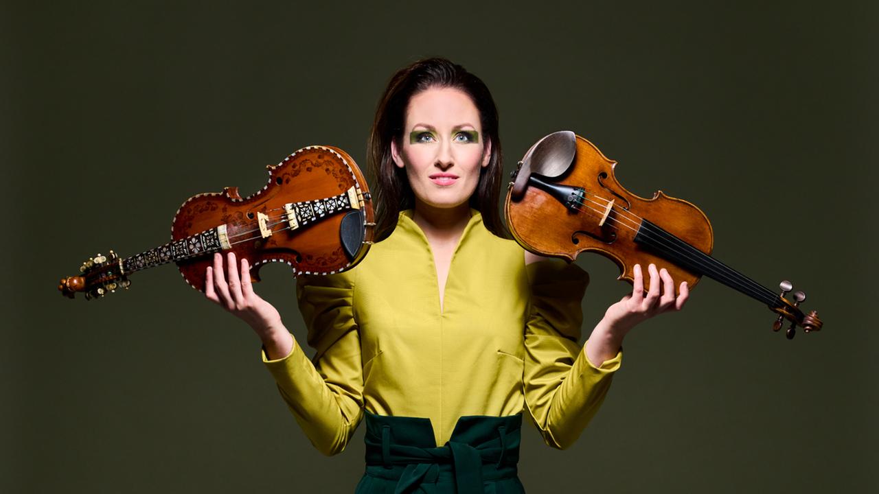 Eine junge Frau trägt ein gelbes Oberteil und einen schwarzen Rock. Sie hält in der linken Hand eine Violine, in der rechten Hand eine Hardangerfidel, dieses Instrument sieht der Geige ähnlich, hat aber viel mehr Verzierungen auf dem Holz.      