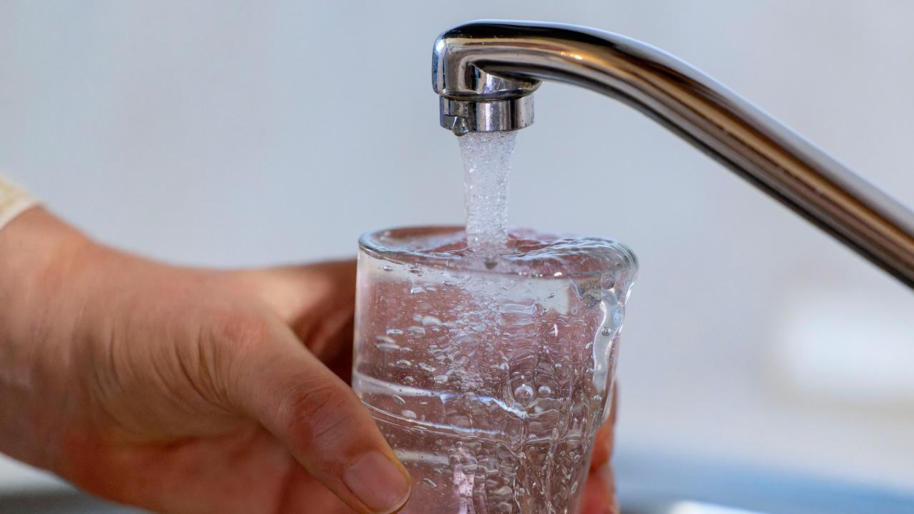 Wasser läuft aus einem Wasserhahn in ein Glas. Eine Hand hält ein Glas unter den Wasserhahn.