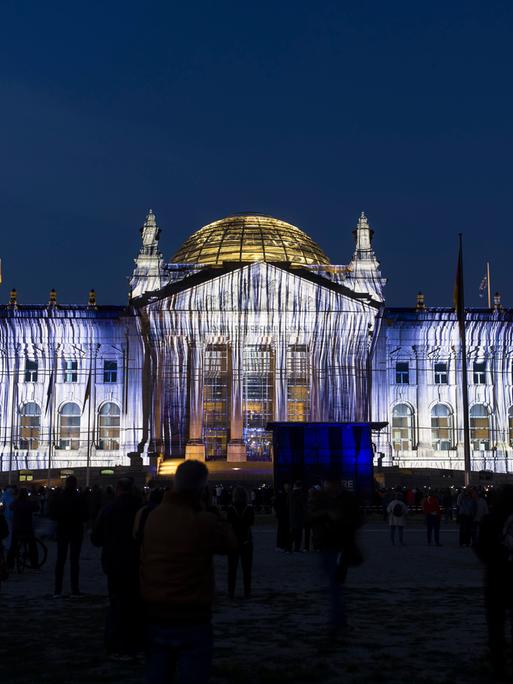 Eine Projektion auf die Westfassade des Reichstags, die aussieht als wäre das Gebäude mit Stoffen behängt. Das Foto wurde bei Nacht aufgenommen. 