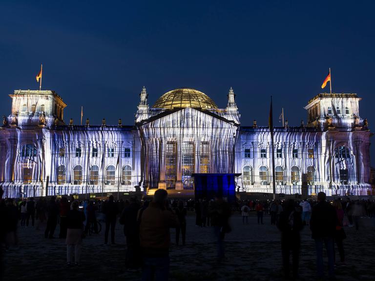 Eine Projektion auf die Westfassade des Reichstags, die aussieht als wäre das Gebäude mit Stoffen behängt. Das Foto wurde bei Nacht aufgenommen. 