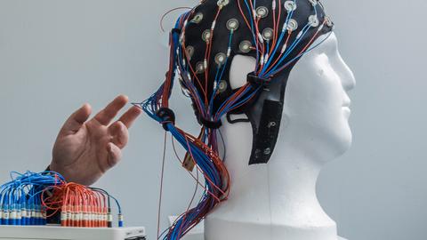 Eine weiße Büste trägt eine Kappe mit angeschlossenen Drähten zur nichtinvasiven Hirnstimulation.
