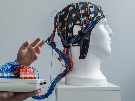 Eine weiße Büste trägt eine Kappe mit angeschlossenen Drähten zur nichtinvasiven Hirnstimulation.