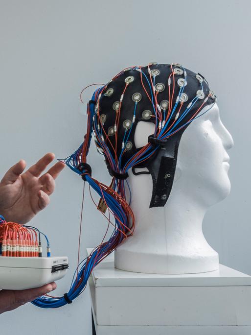 Eine weiße Büste trägt eine Kappe mit angeschlossenen Drähten zur nichtinvasiven Hirnstimulation.