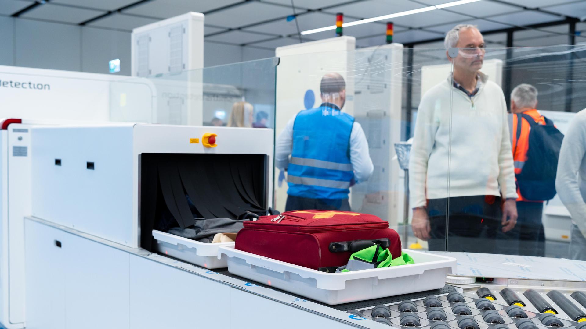 Passagiere warten im Flughafen München darauf, dass ihr Handgepäck über das automatische Kontrollband zur Sicherheitsprüfung weiterläuft.