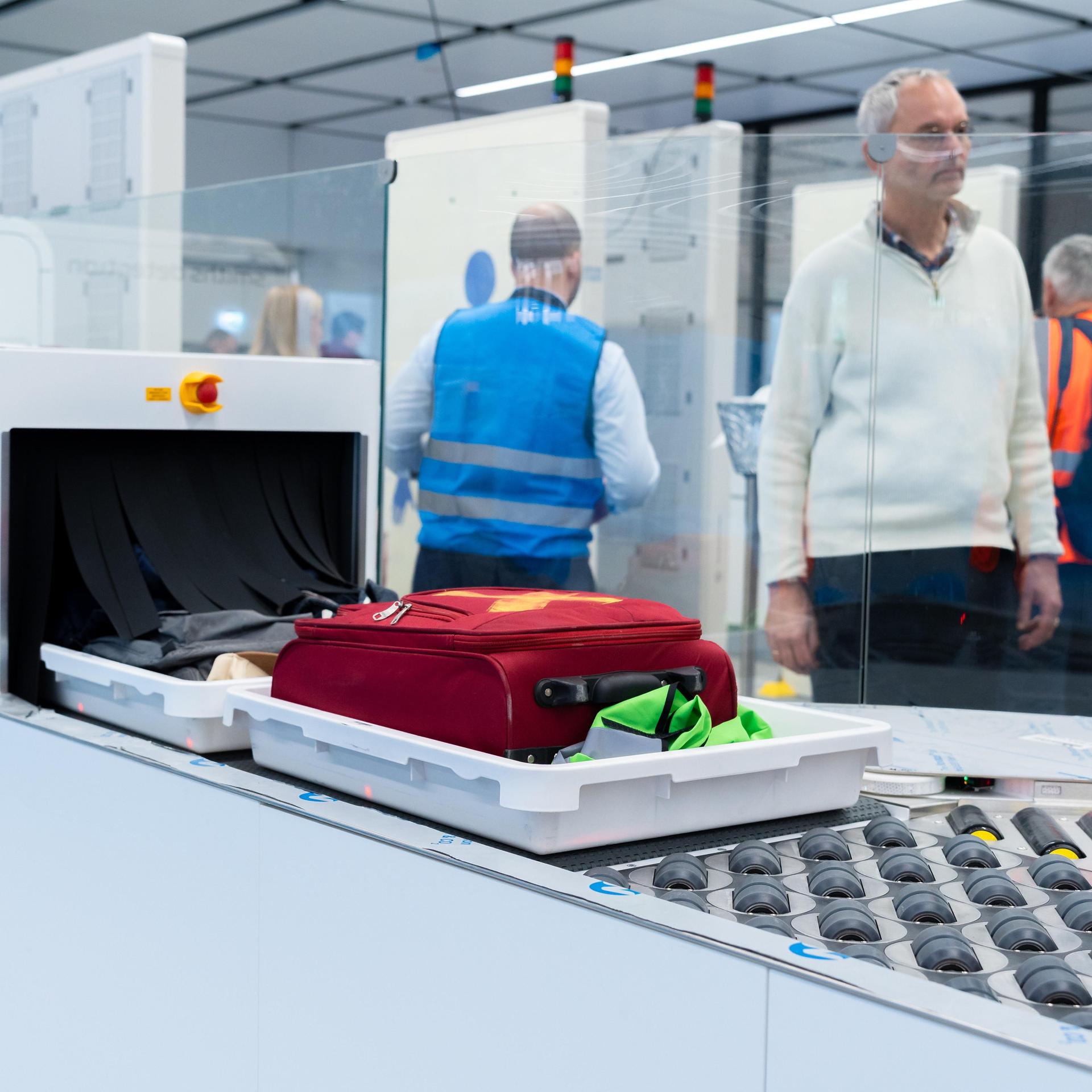 Passagiere warten  im Flughafen München darauf, dass ihr Handgepäck über das automatische Kontrollband zur modernen Sicherheitsprüfung weiterläuft.