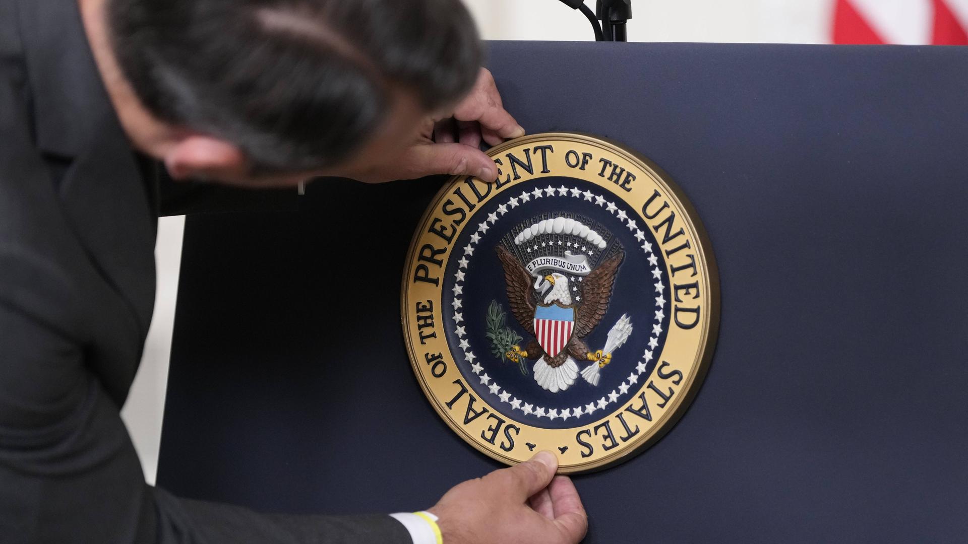 Ein Mitarbeiter der US-Regierung bringt das Siegel des US-Präsidenten an dessen Rednerpult an. 