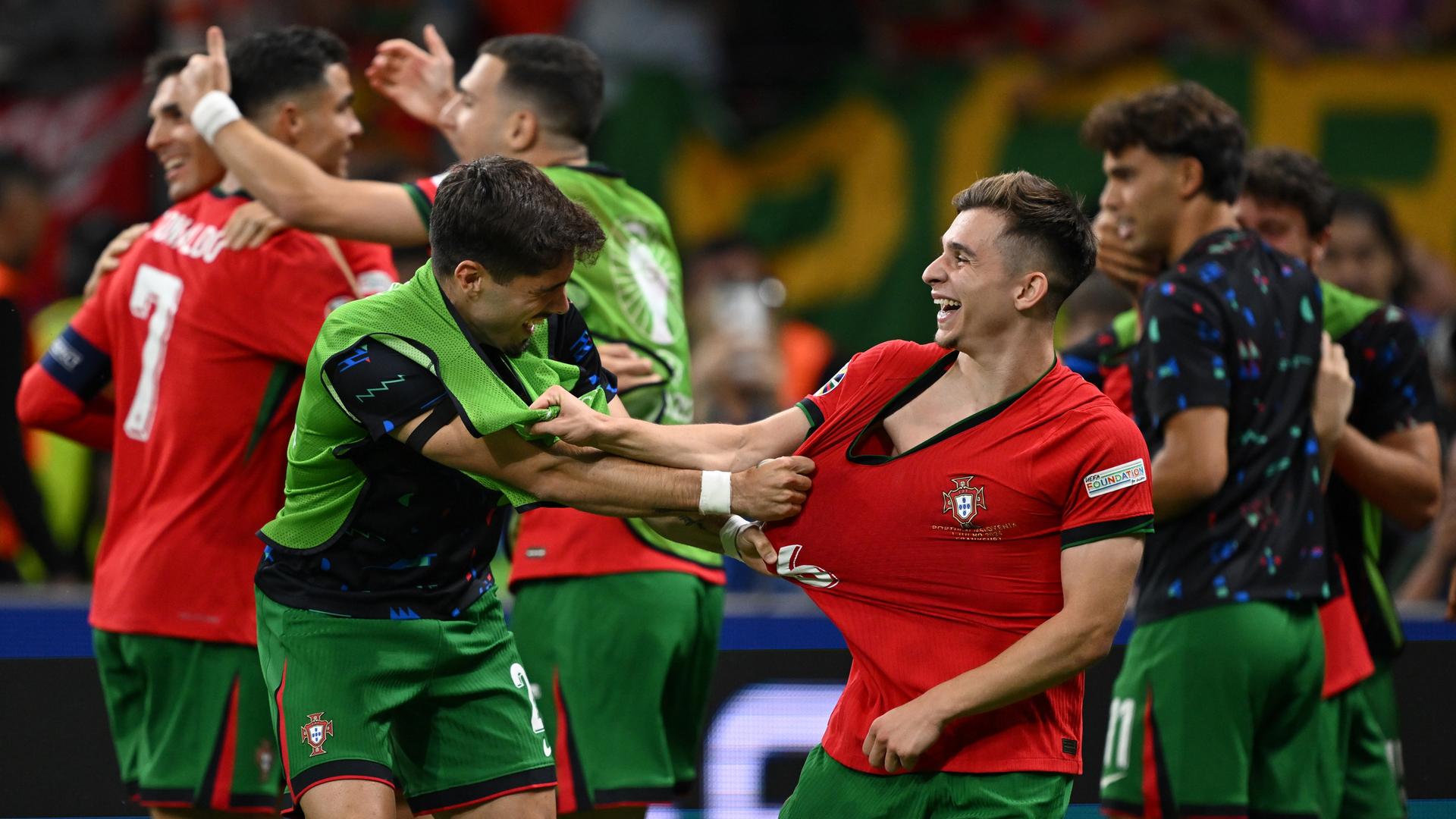 Ein Ersatzspieler mit grüner Warnweste zieht freudig am roten Trikot des Spielers  Francisco Conceiçãos (rechts vorne), der lacht. Dahinter feiern weitere Spieler den Sieg. 