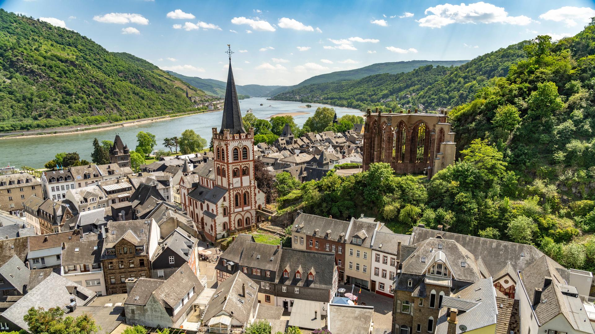 Über der Altstadt von Bacharach ragen die Evangelische Kirche St. Peter und die gotische Wernerkapelle auf. Im Hintergrund sind der Rhein und bewaldete Hügel zu sehen.