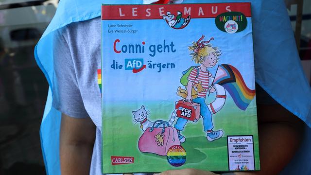 Ein Buch mit dem Titel "Conni geht die AfD ärgern". Auf dem Titel ist ein blondes Mädchen mit rot-weiß-geringeltem T-Shirt. Es trägt eine Regenbogenfahne. 