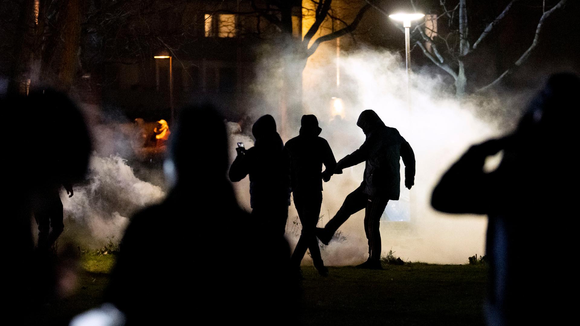 Demonstrierende nachts auf einer Straße im schwedischen Malmö. Sie sind als dunkler Schattenriss im Nebel von Tränengas zu sehen.