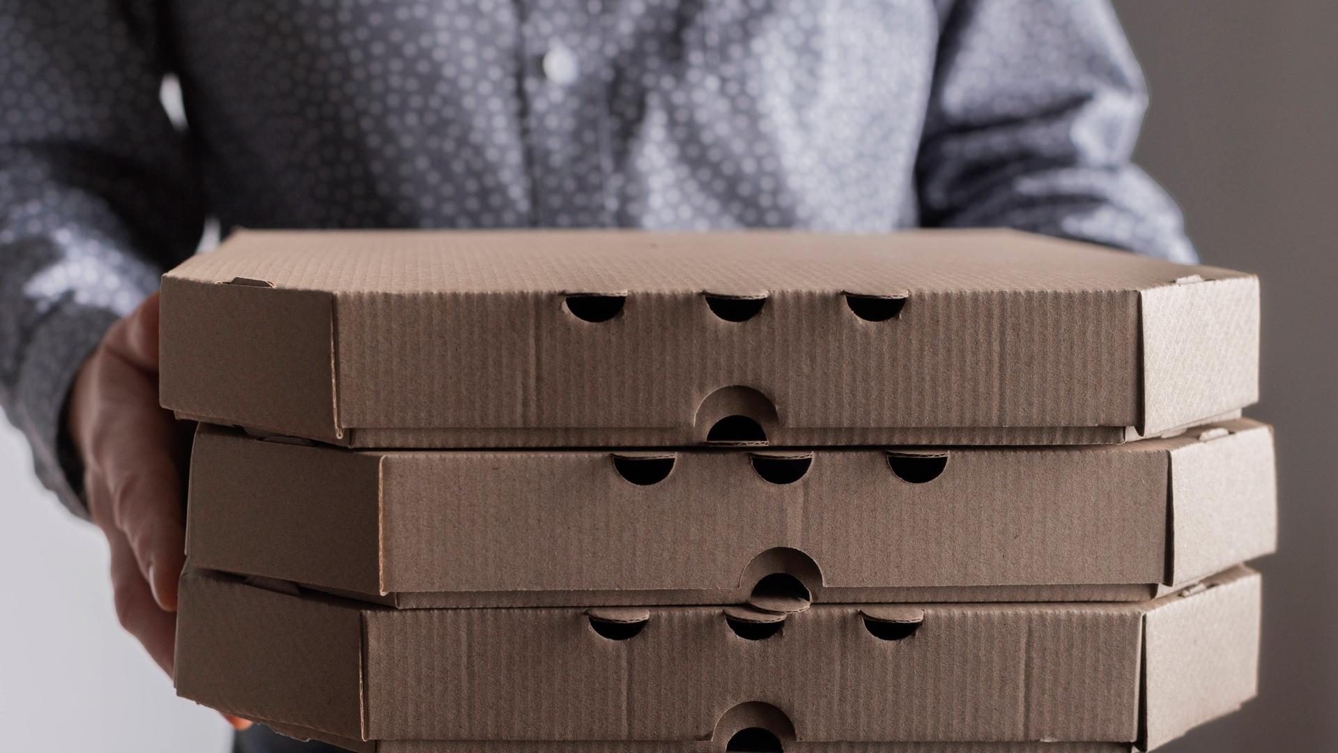 Ein Mann hält drei Pizzkartons in der Hand.