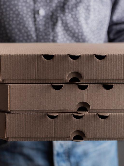 Ein Mann hält drei Pizzkartons in der Hand.