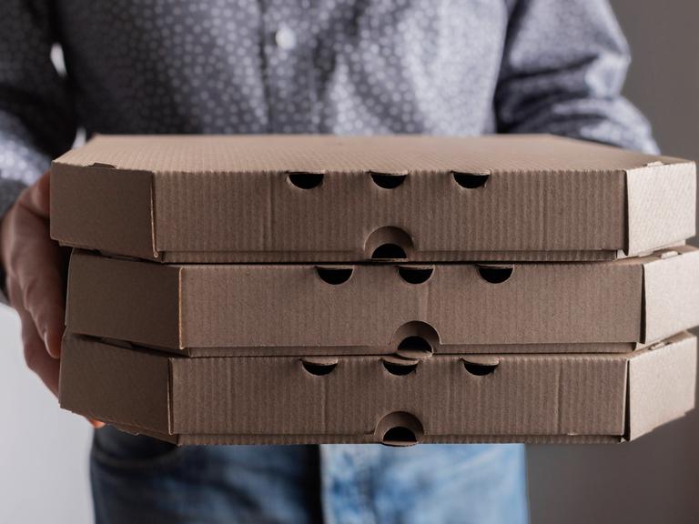 Ein Mann hält drei Pizzkartons in der Hand.