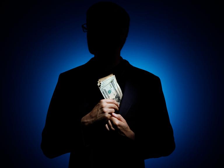 Silhouette eines Mannes vor blauem Licht, der sich ein Bündel Geldscheine in das Sakko steckt.