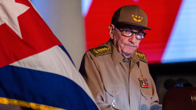 Ein alter Mann mit Brille und in Uniform - es ist Raúl Castro. Er sitzt neben einer kubanischen Flagge.