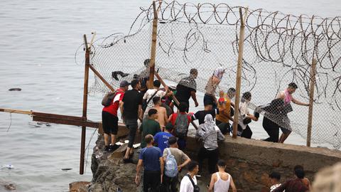 Eine Gruppe Migranten flüchtet durch einen Zaun an der marokkanisch-spanischen Grenze am 31.Juli 2026. Sie klettern durch ein Loch im Zaun am Hafen in die Spanien-Exklave Ceuta.