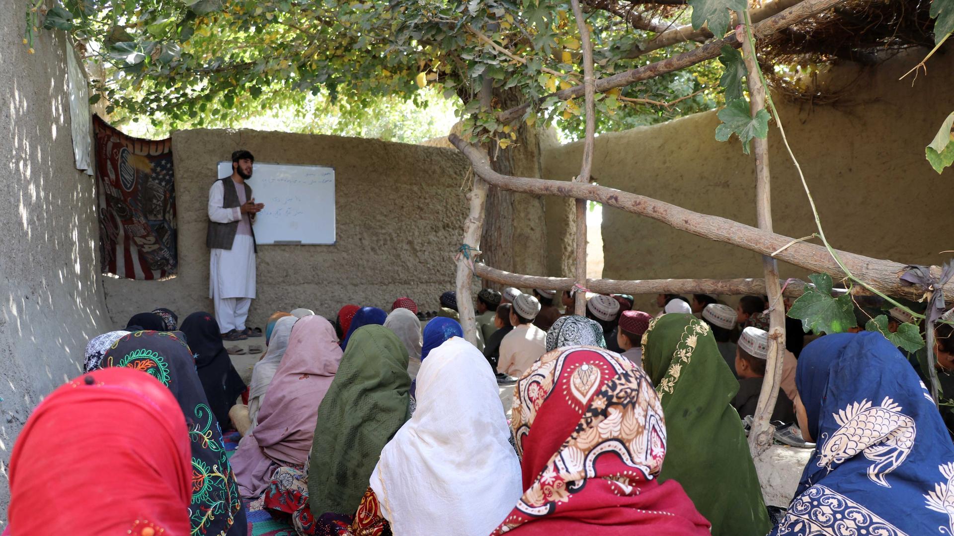 Ein Afghane unterrichtet Mädchen und Jungs in einem afghanischen Dorf. Die Schülerinnen und Schüler sitzen auf dem Boden. Ein Afghane unterrichtet Mädchen und Jungs in einem afghanischen Dorf. Die Schülerinnen und Schüler sitzen auf dem Boden.