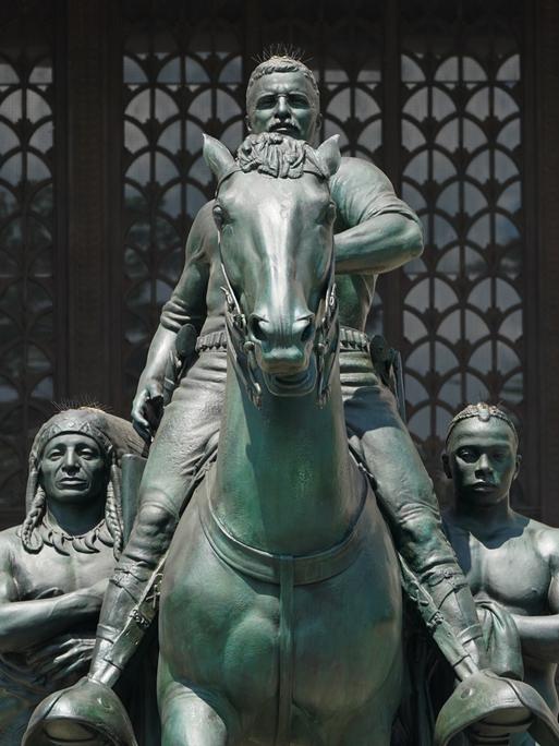 Ein Denkmal zu Ehren von Theodore Roosevelt vor dem Eingang des New Yorker Naturkunde Museums entfernt. Es zeigt ihn in heroischer Pose zu Pferd, flankiert von zwei hemd- und namenlosen Waffenträgern: einem indigenen und einem schwarzen Mann. 