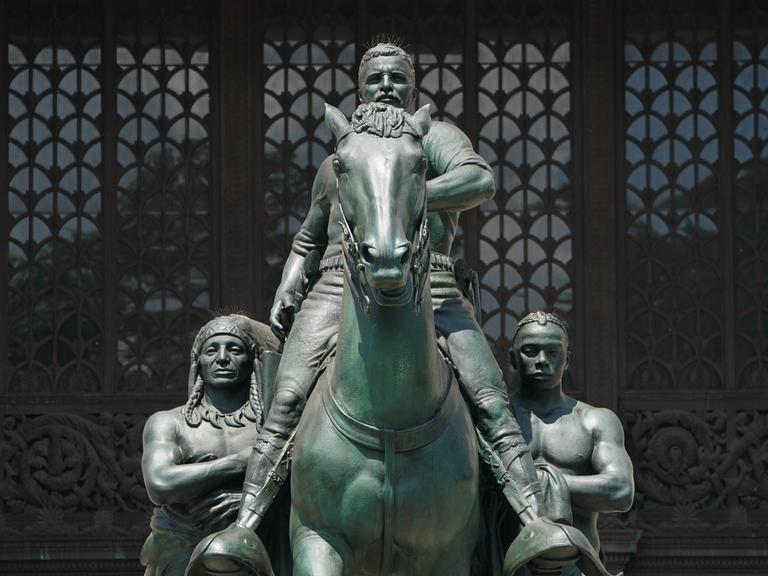 Ein Denkmal zu Ehren von Theodore Roosevelt vor dem Eingang des New Yorker Naturkunde Museums entfernt. Es zeigt ihn in heroischer Pose zu Pferd, flankiert von zwei hemd- und namenlosen Waffenträgern: einem indigenen und einem schwarzen Mann. 