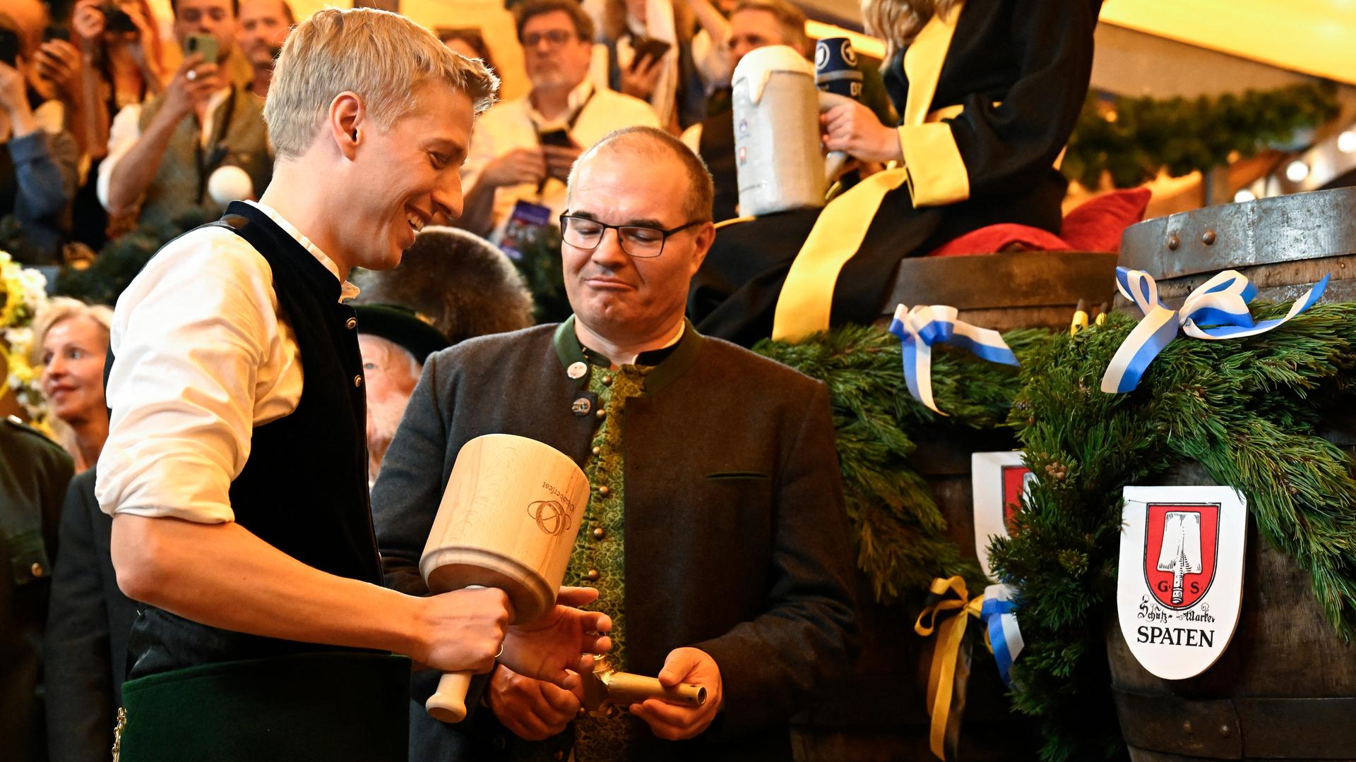 Krause steht im Festzelt und hat einen Hammer in der Hand. Neben ihm siond mehrere Fässer Bier zu sehen. Krause steht im Festzelt und hat einen Hammer in der Hand. Neben ihm siond mehrere Fässer Bier zu sehen.
