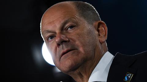 Bundeskanzler Olaf Scholz in Nahaufnahme vor schwarzem Hintergrund. Er dreht den Kopf nach links und blickt ernst.