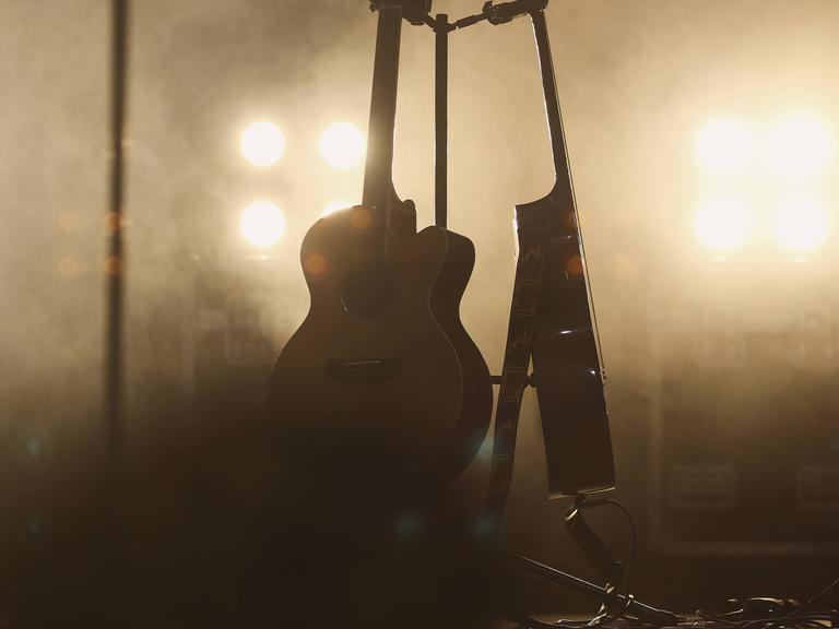 Zwei Gitarren stehen im Bühnennebel. Von hinten leuchten Scheinwerfer.