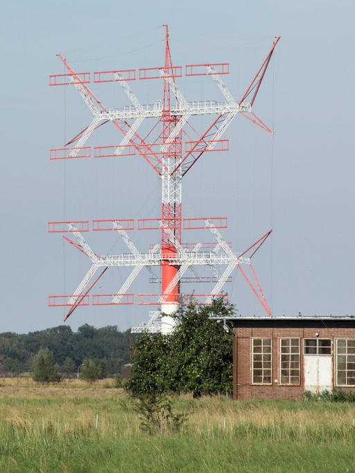 Das Bild zeigt eine in den Farben Rot und Weiß gehaltene große Kurzwellenantenne. Bezüglich der Bauart in Gitterstruktur erinnert das Gebilde an einen Strommast. 