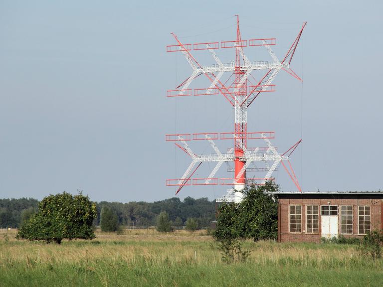 Das Bild zeigt eine in den Farben Rot und Weiß gehaltene große Kurzwellenantenne. Bezüglich der Bauart in Gitterstruktur erinnert das Gebilde an einen Strommast. 