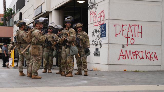 Soldaten stehen neben einem Gebäude. Auf die Wand von dem Gebäude hat jemand, "Tod für Amerika" geschmiert.